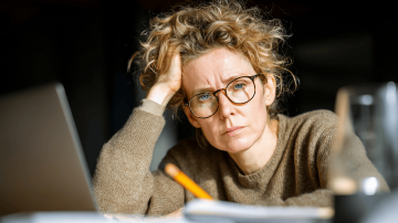 Žena sedí u počítače se zamračeným výrazem, hlavu si podpírá rukou